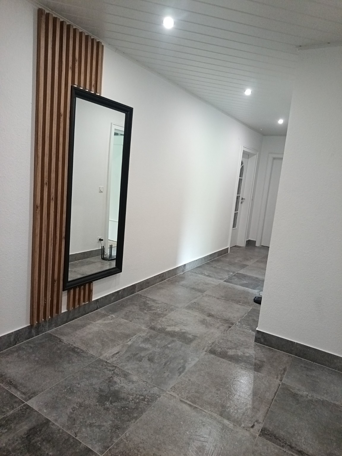 Corredor reformado con pavimento cerámico gris, rodapiés y panel decorativo de madera